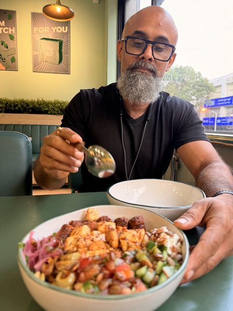 Venky raising a spoon over a large bowl of grain salad in a caf&eacute;.